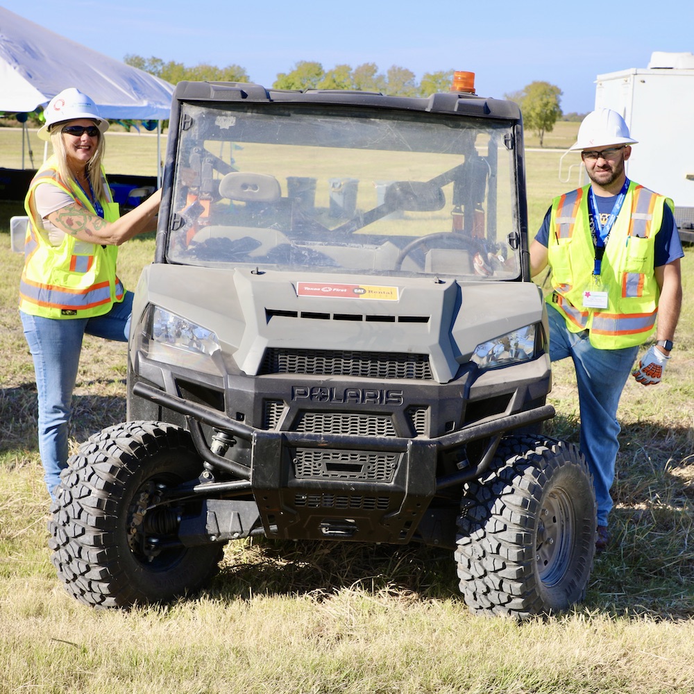 Man and woman in construction clothing and and hard hats next to all-terrain vehicle