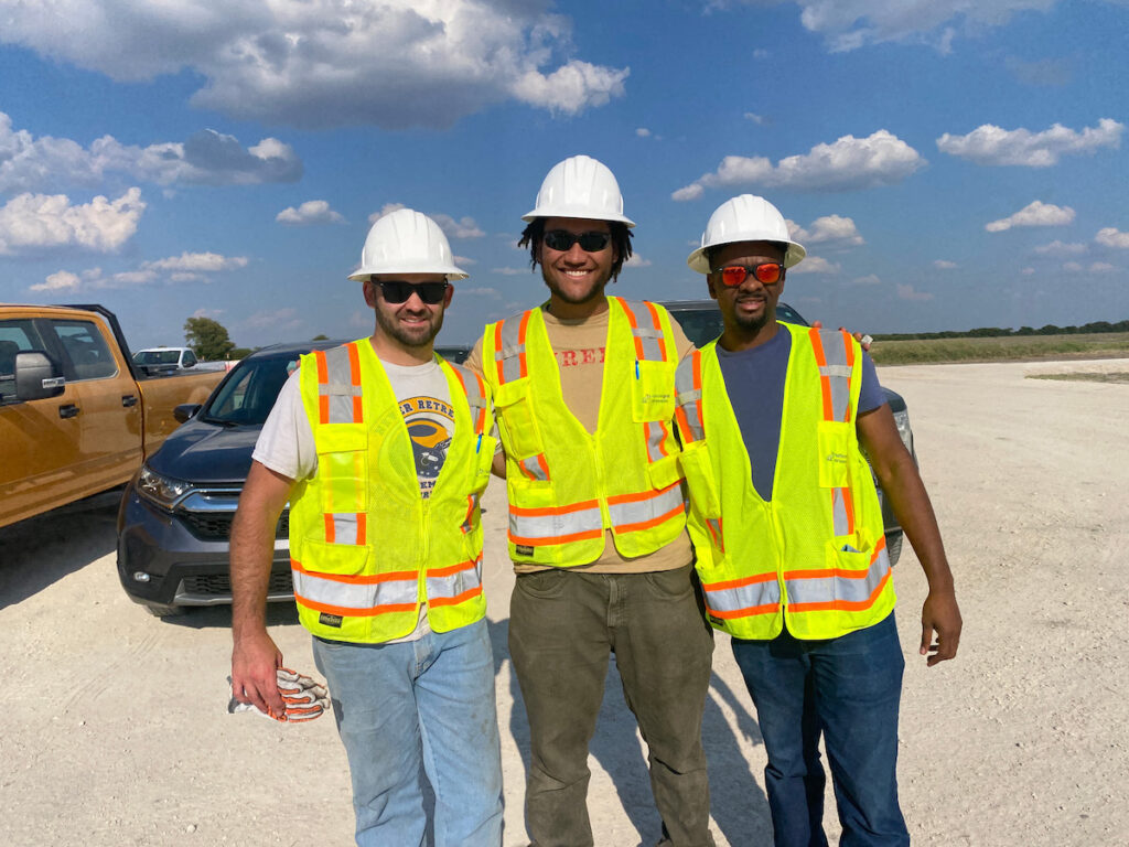 Three people in construction helmets and vests